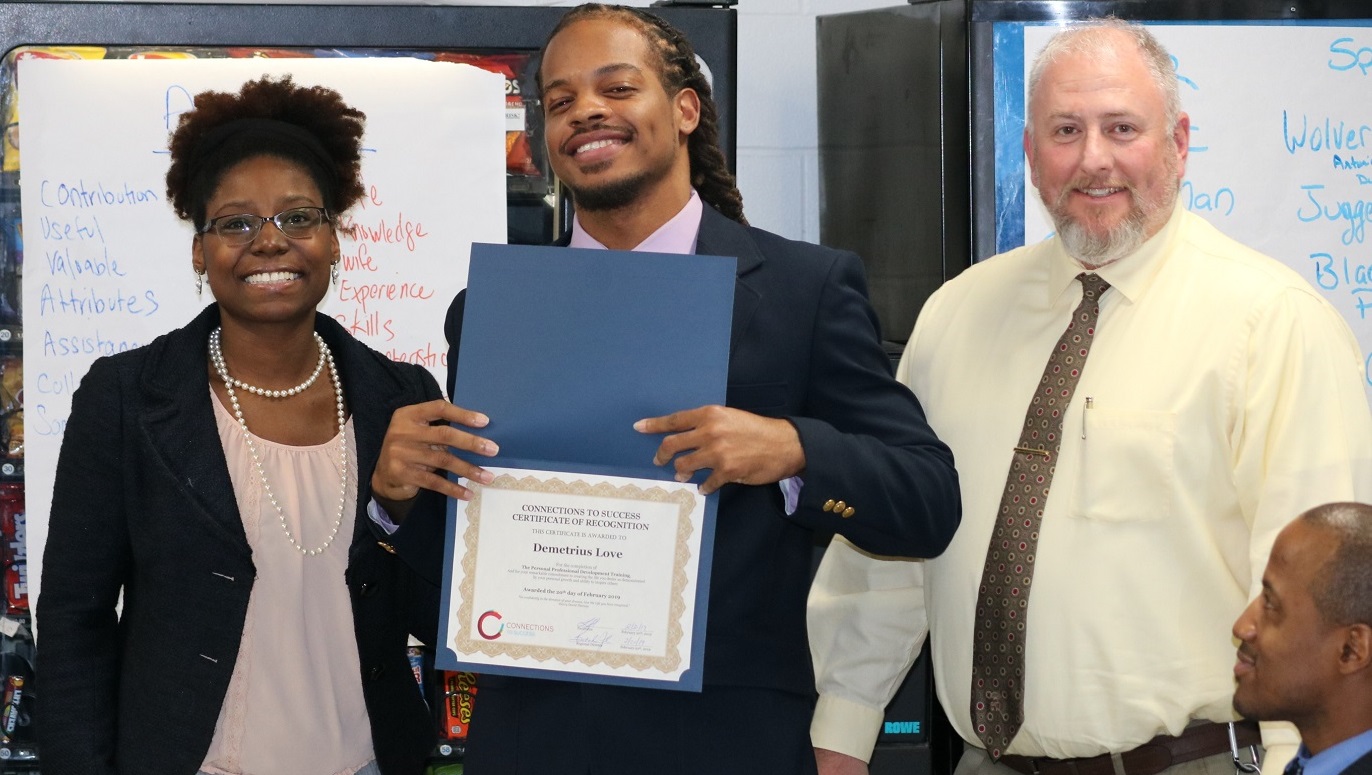 An offender holding a diploma poses with two staff members.