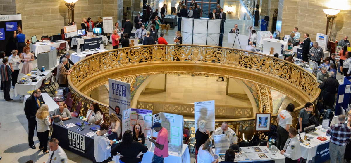 Group of people and exhibits stationed round the rotunda in the Missouri State Capitol building