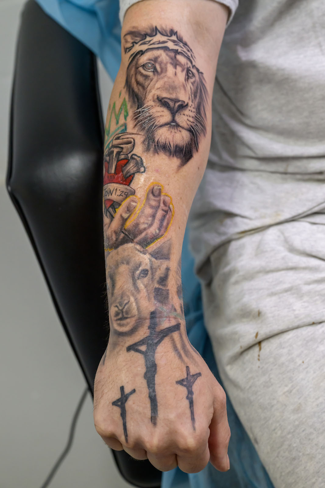 Man shows arm tattoo featuring lion, lamb and a crucifixion scene.
