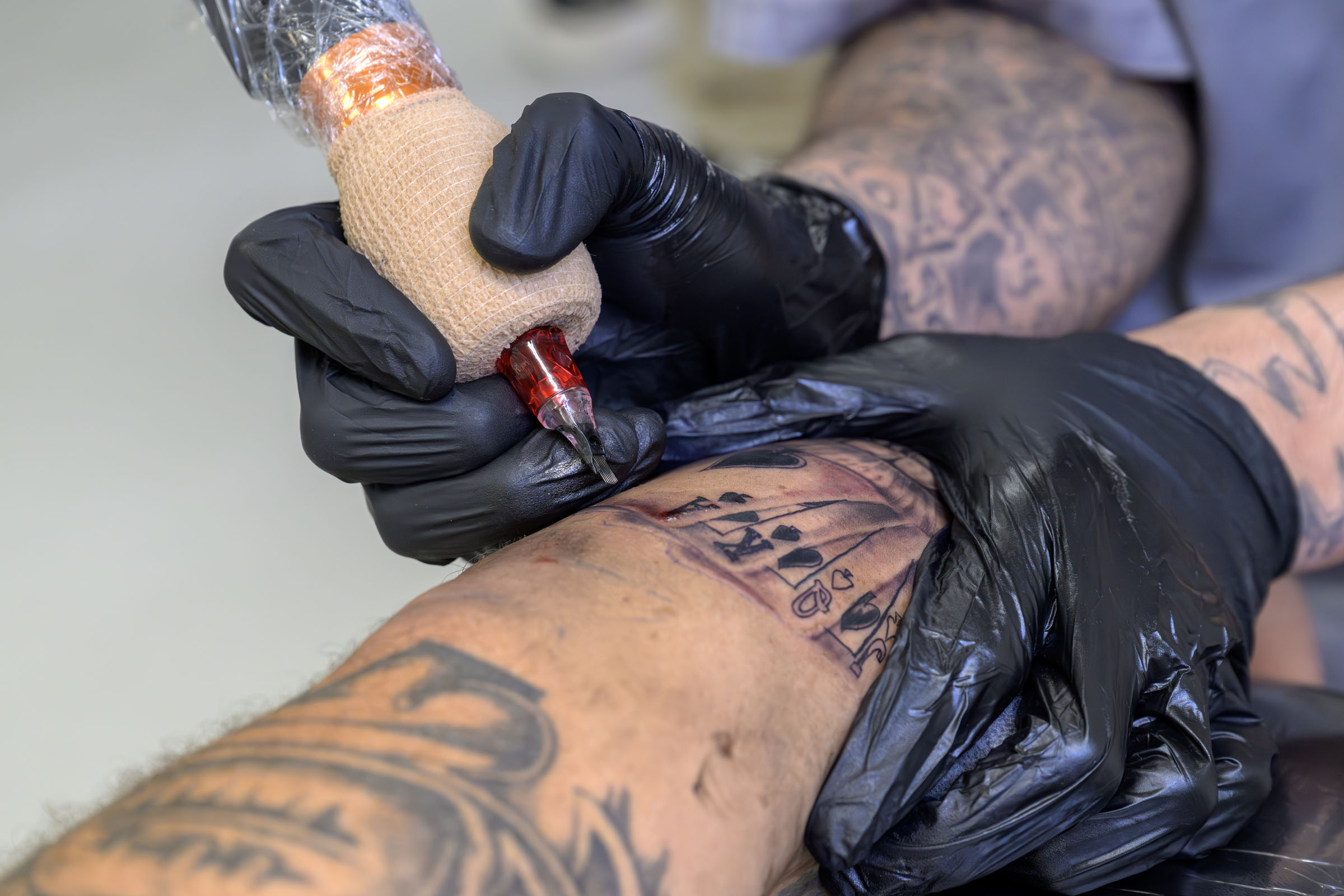 Detail showing artist tattooing playing cards on client’s arm.