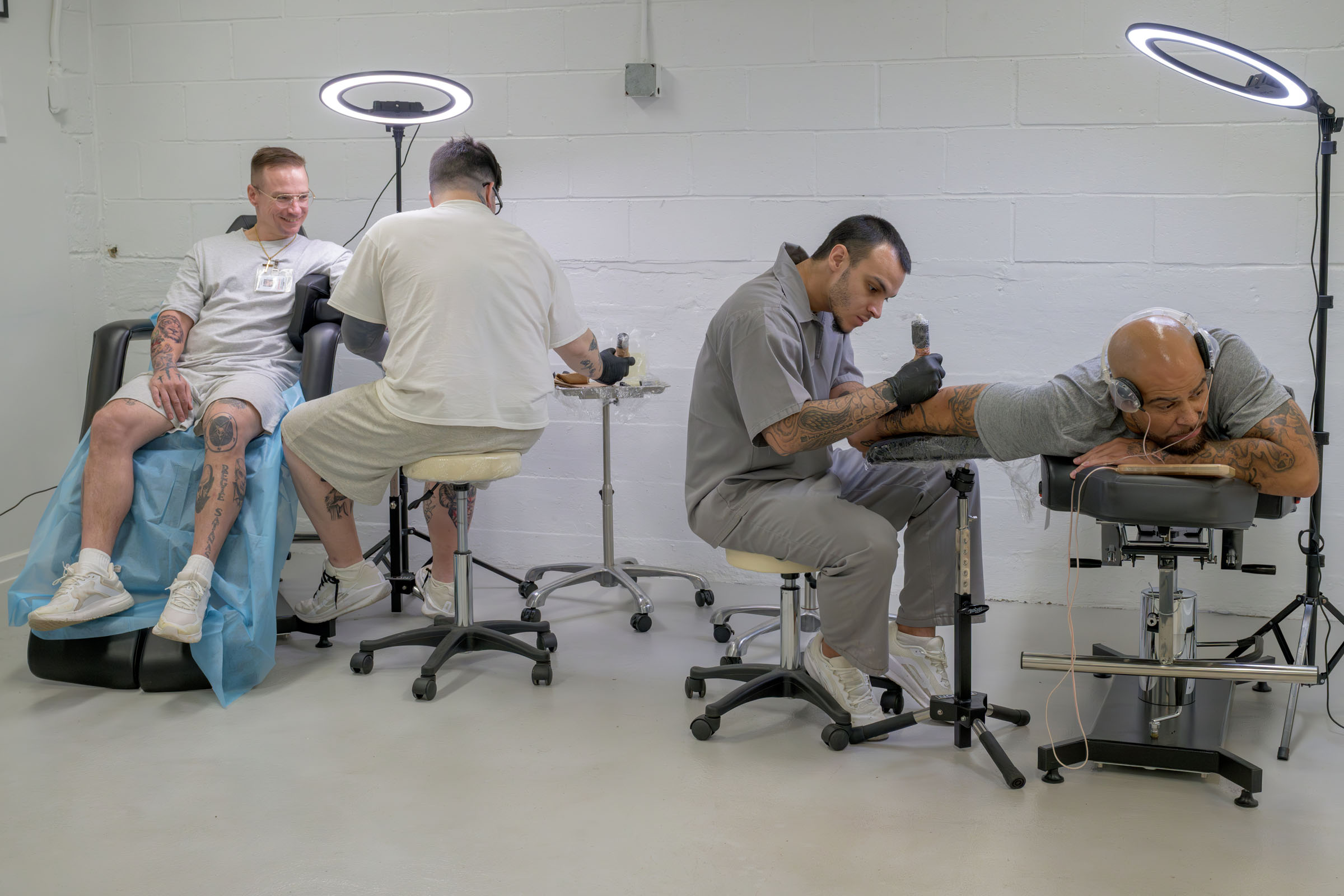 Two artists work simultaneously work on the tattoos of two clients.