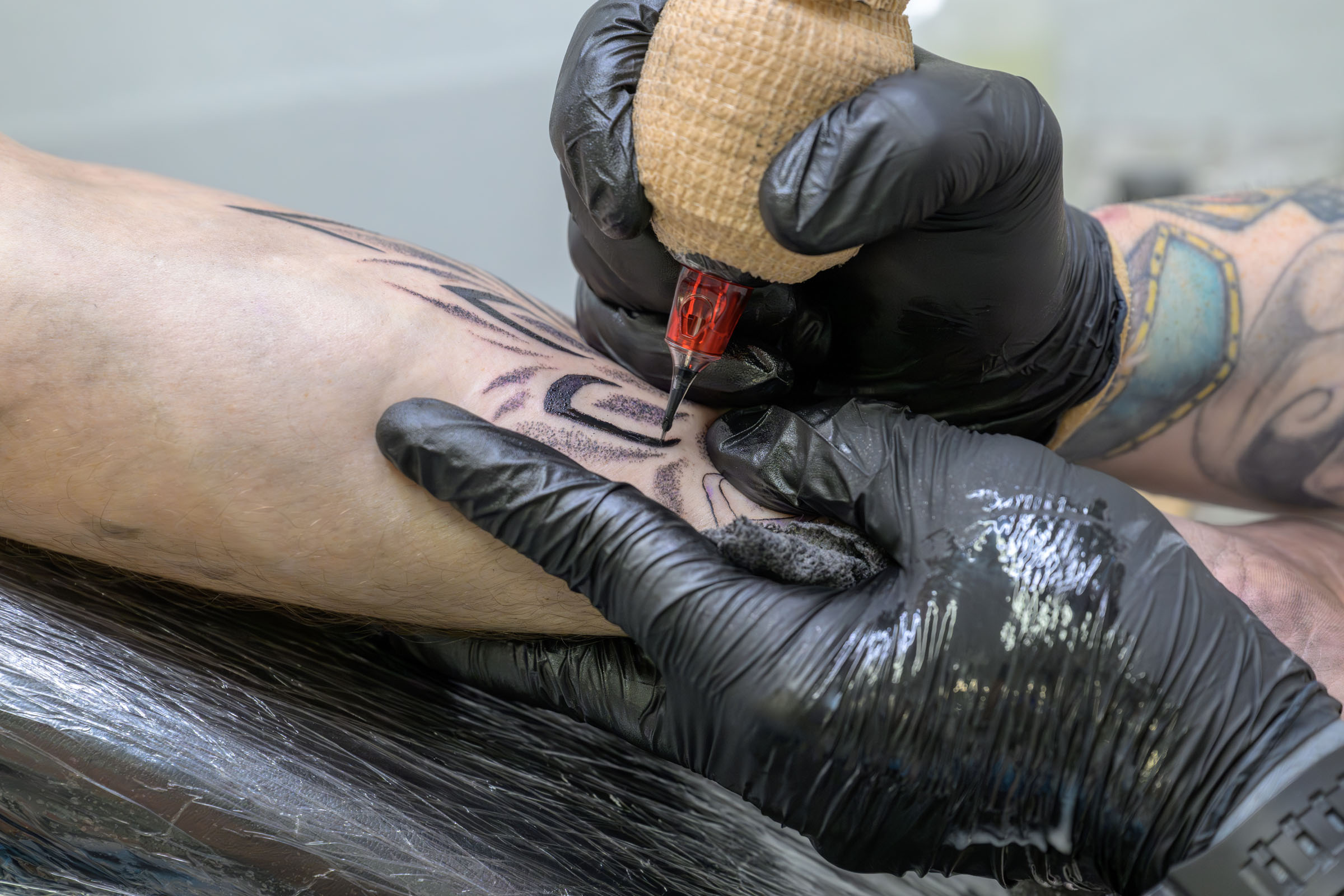 Detail showing artist tattooing a mandala on client’s arm.