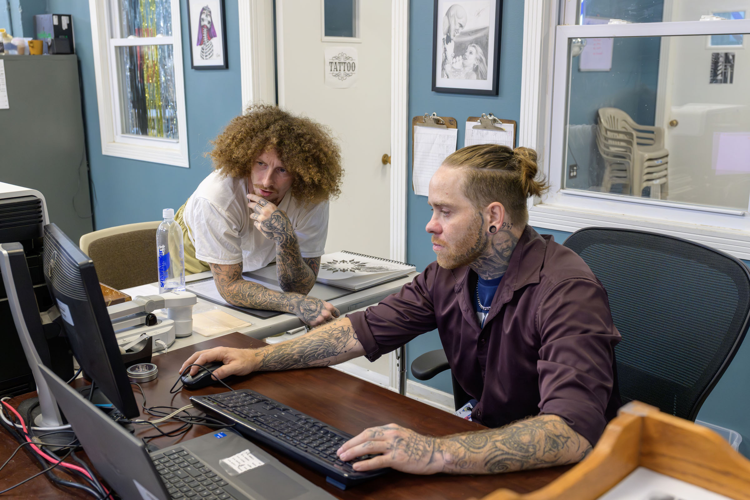 Student looks over the shoulder of his teacher at a computer monitor.