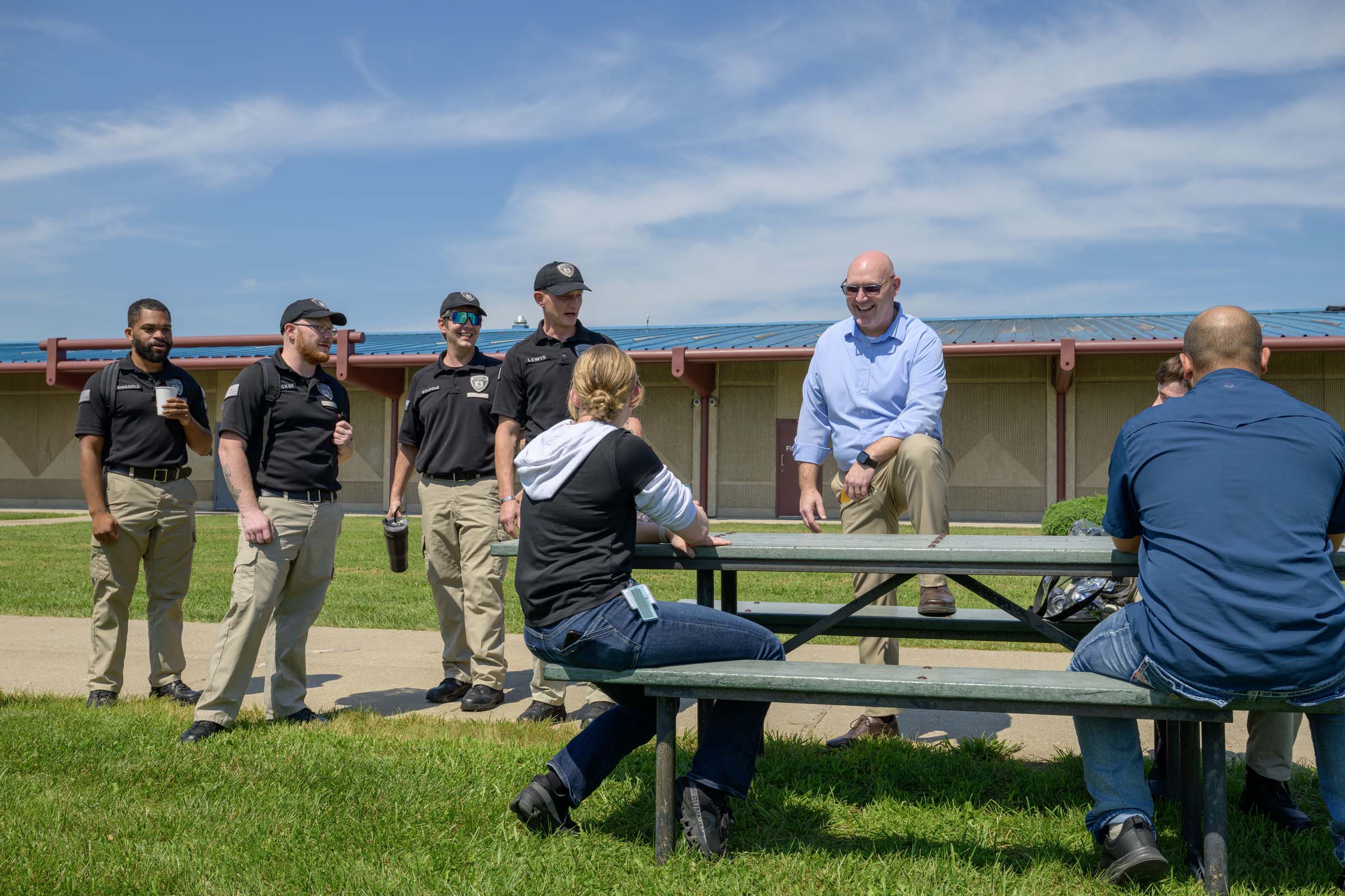 Ryan Brownlow stands with a leg up on a picnic bench and laughs with a group of cadets.