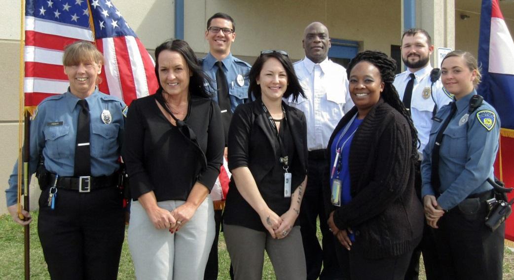 Group of corrections officers in uniform standing by a U.S. flag.