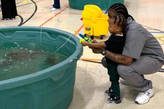A dad shows his toddler how to catch a fish in a pool