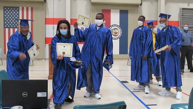 Students in caps and gowns showing diplomas to computer camera