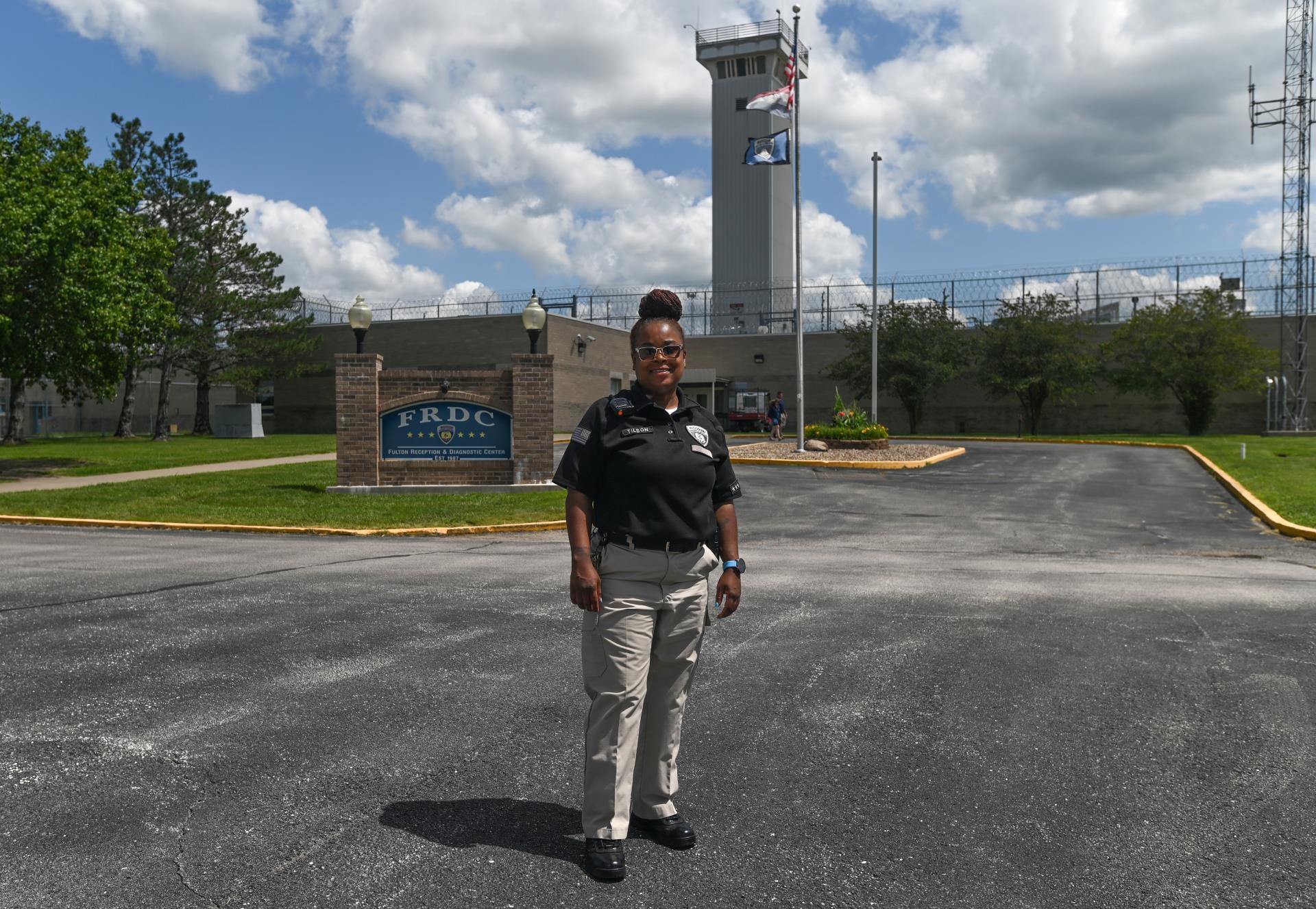 A female correctional officer stands in front of a facility