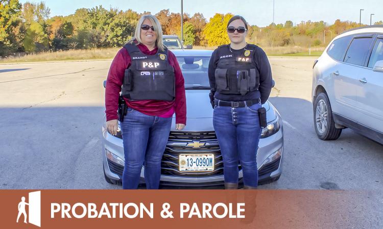 Two Probation and Parole officers pose in front of car with a graphics overlay that says Probation and Parole.